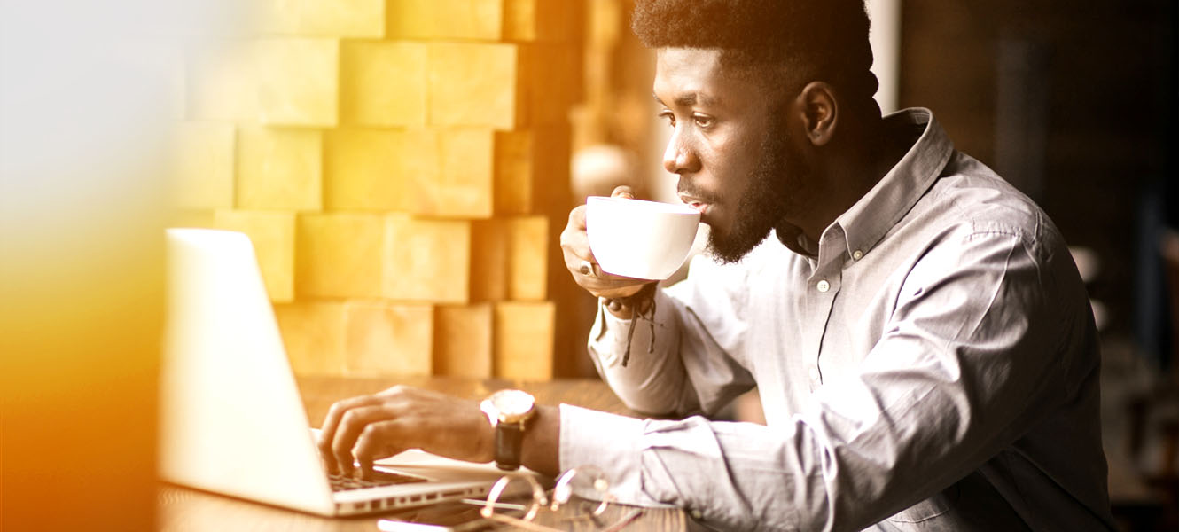 Young man one his lap top drinking coffee out of a cup.